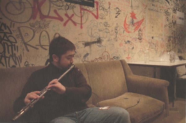 nujabes jouant de la flûte sur un canaper dans une loge d'une salle de concert